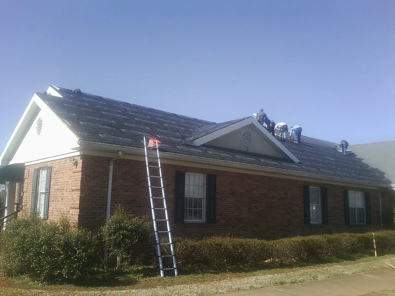 Crew tearing shingles off a brick ranch roof with a ladder set — Metal Roof Repair work by our crew in Niles