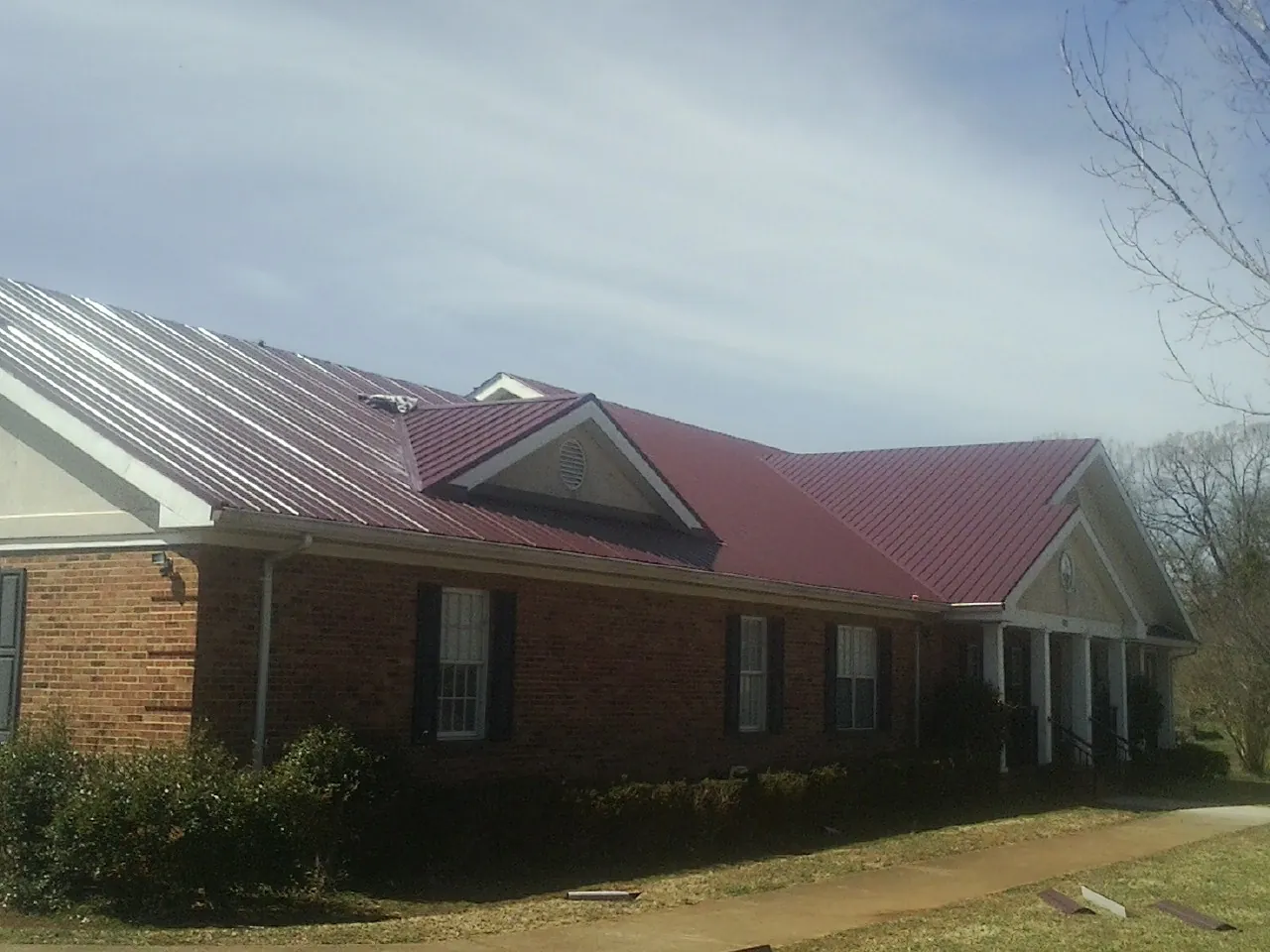 Red metal roof with gabled entries on a long brick building, from a Hail Damage Roof Repair job in Niles