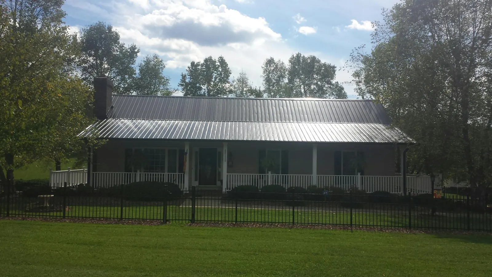 Gray metal roof on a brick ranch with a full width front porch — Gutter Guard Installation work by our crew in Niles
