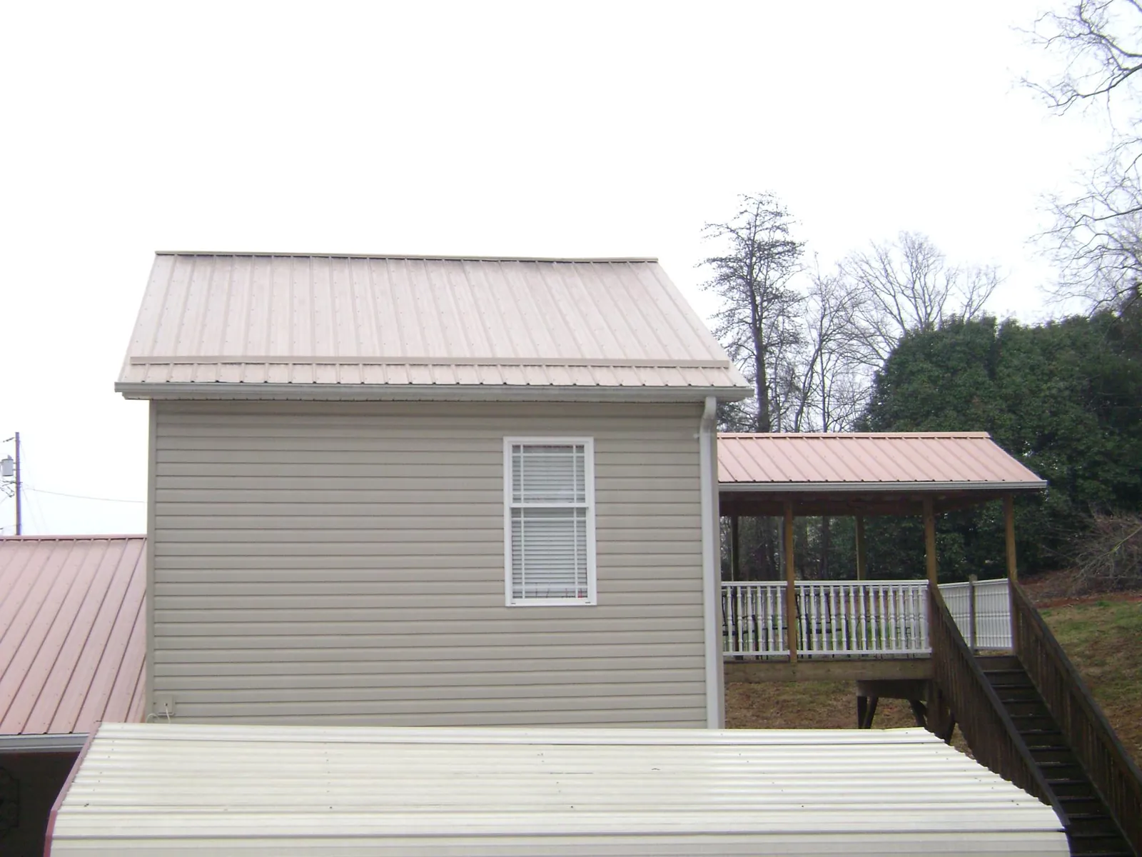 Tan metal roofs on a two story addition and attached porch, from a Roof Replacement job in Niles